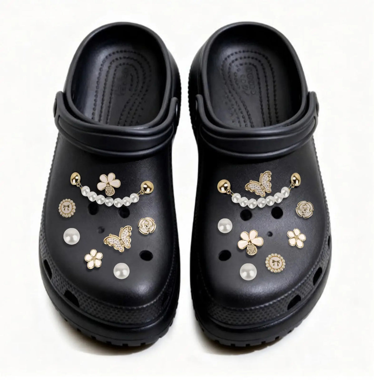 Un par de charm para zapatos negros con diseños florales y de mariposa de diamantes dorados y blancos.