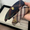 A close-up of two British plaid sponge headbands, one dark blue and another beige, displayed in a black box.
