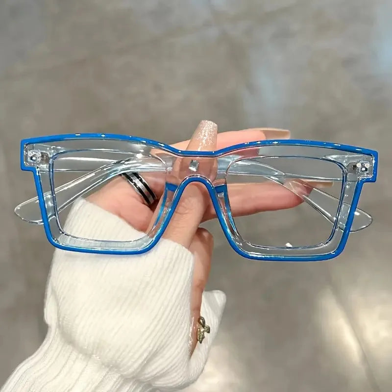 A hand holds a pair of clear square frame costume glasses with blue accents against a light background.