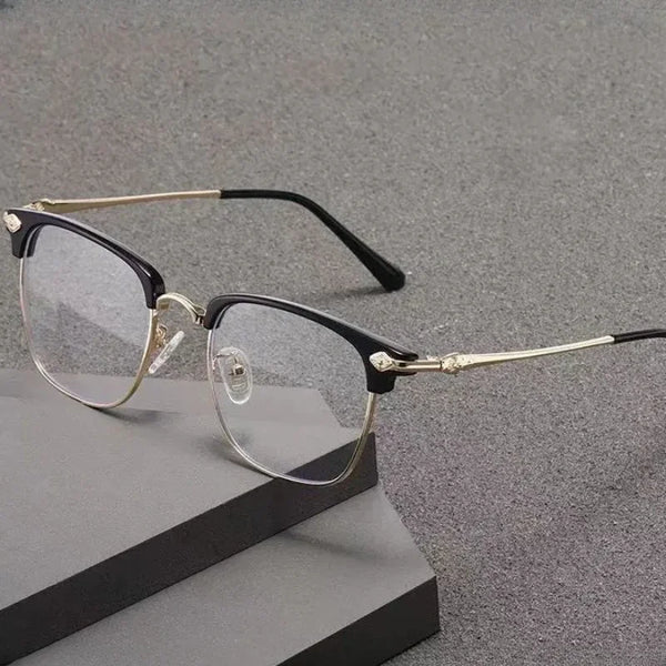 A pair of black and gold metal half-frame reading glasses resting on a dark gray surface.