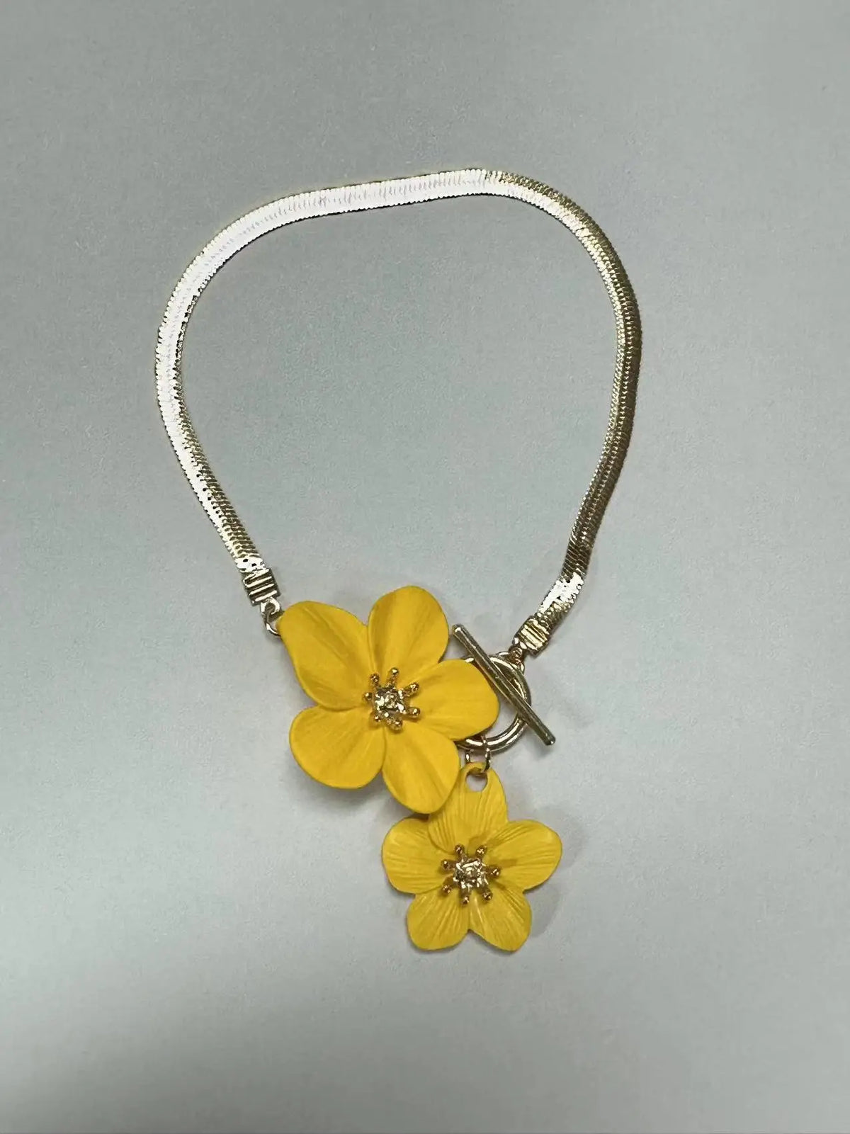 A gold-toned chain necklace with a yellow floral pendant and matching earring.