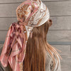 A woman wearing a pink and beige silk print shawl wrapped around her head, viewed from the back.