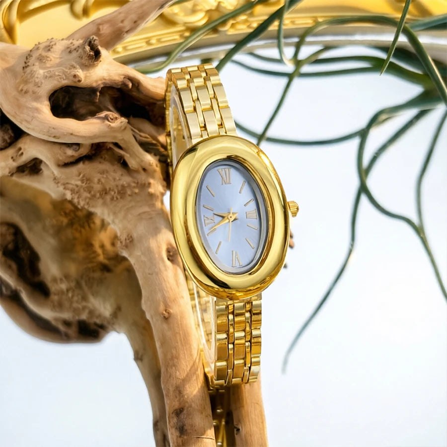 Reloj vintage dorado con esfera azul claro y manecillas plateadas, mostrado en un cráneo de madera.
