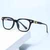 Black square eyeglasses with gold accents resting on a white surface.