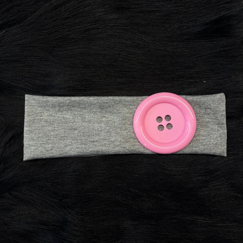 A pink silicone hairband with small holes is placed on a gray fabric band against a black background.