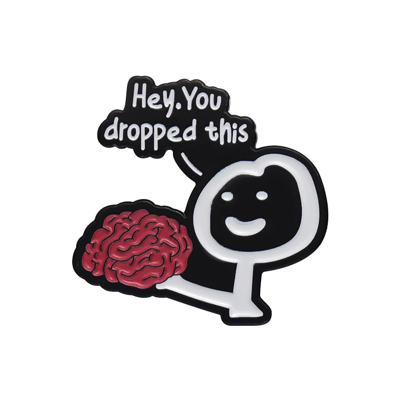 Insignia de esmalte negro con un gráfico estilizado de cerebro y el texto "Hey You dropped this"