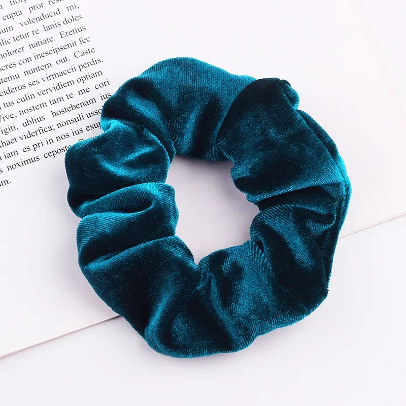 A dark teal velvet scrunchie is shown against a white background.