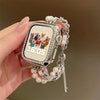A close-up of a smartwatch with a square display and a silver beaded watch strap being held by a hand.