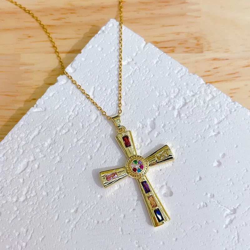 A gold-colored cross charm necklace with colorful gemstone accents displayed on a white surface.