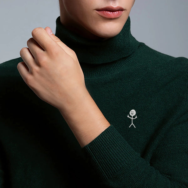 Close-up of a person wearing a dark green turtleneck sweater with a white stickman brooch on the chest.