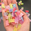 A hand holds a pile of colorful resin nail art charms in various shades of pink, purple, yellow, and green.