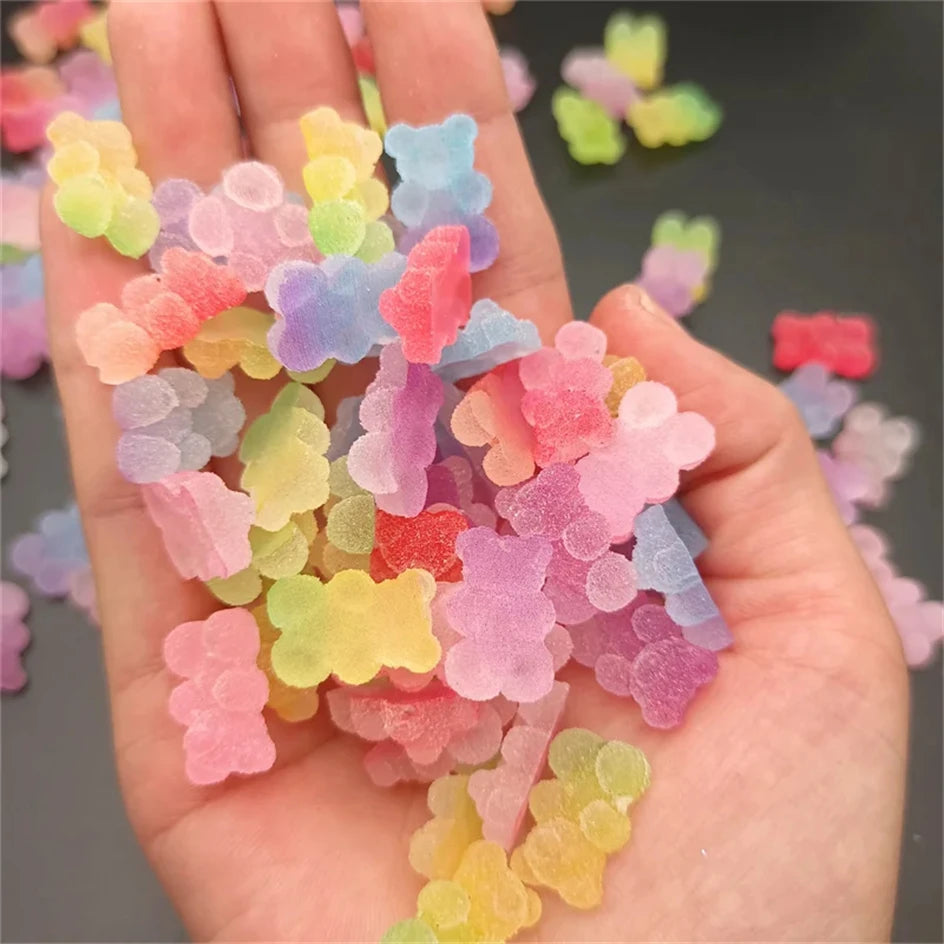 A hand holds a pile of colorful resin nail art charms in various shades of pink, purple, yellow, and green.