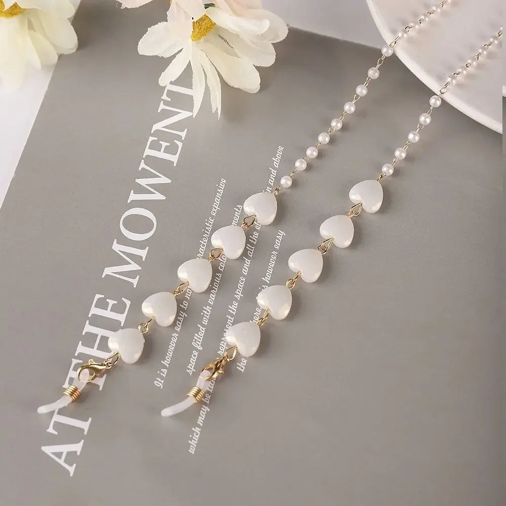 A delicate gold and pearl beaded eyewear chain displayed on a gray background with white flowers.