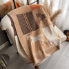 A beige and orange plaid cashmere feel scarf draped over a black metal hanger.