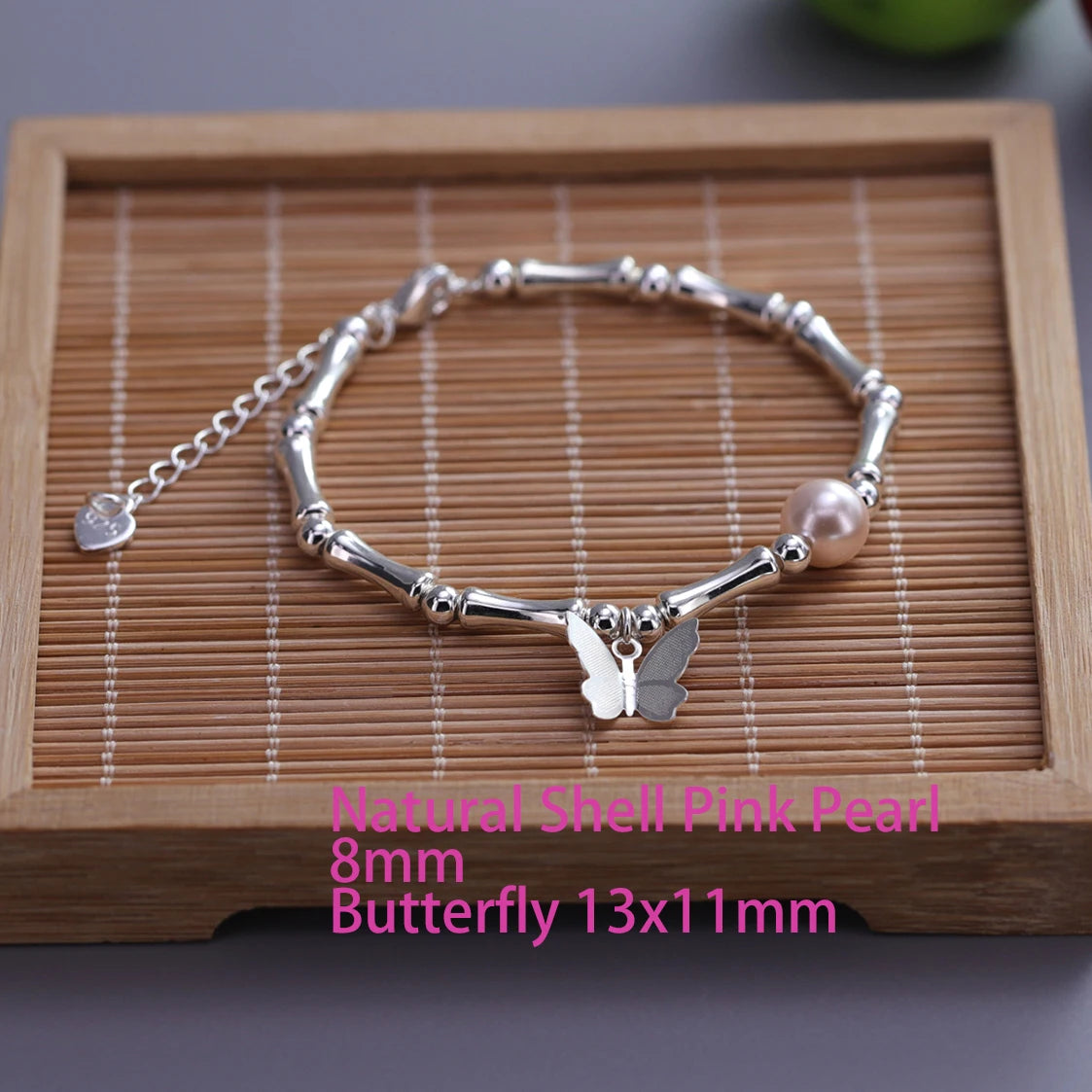 Sterling silver double heart charm bracelet with pink pearl and butterfly pendant displayed on a wooden board