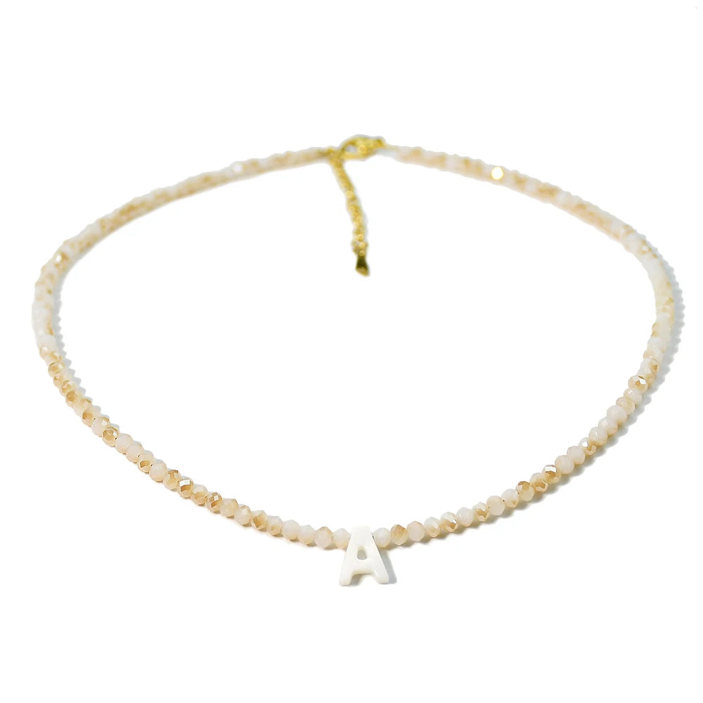 A delicate mother of pearl initial necklace featuring crystal accents and a gold-colored cord.