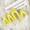 Pinzas para el pelo de gel amarillo en forma de ola sobre papel blanco arrugado con una cita.