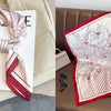 A red and white striped silk scarf with a floral print is displayed on a white card and draped on a brown leather sofa.