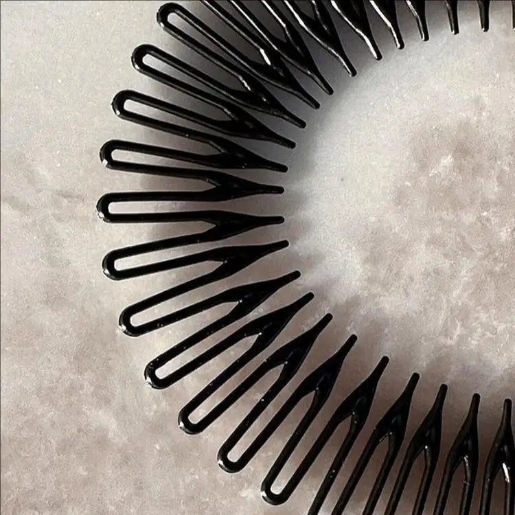 Gros plan d'une pince à cheveux en plastique noir, stretch, avec de fines tiges, sur une surface claire.