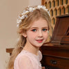 A young girl with long blonde hair wears an elegant floral wreath headband and a pink dress.