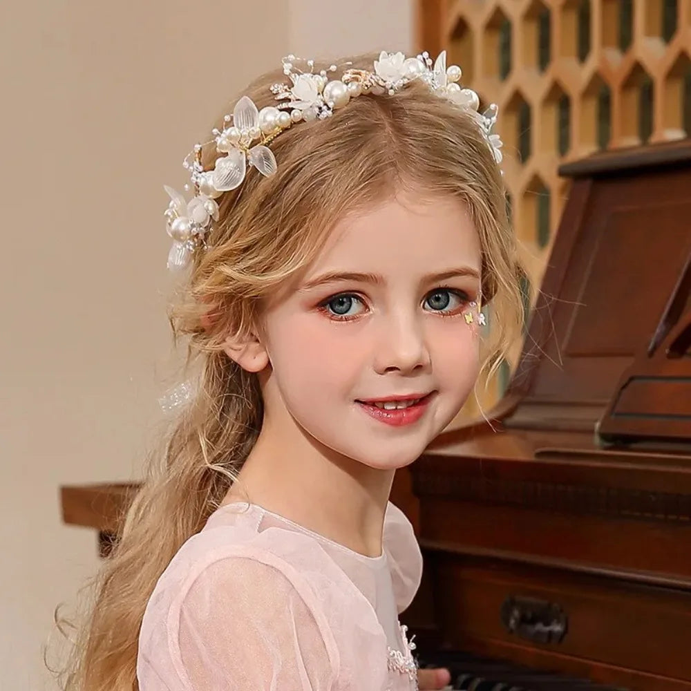 A young girl with long blonde hair wears an elegant floral wreath headband and a pink dress.