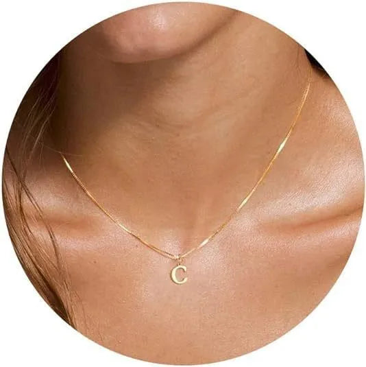 A close-up of a gold plated alphabet initial necklace resting on a person's neck.