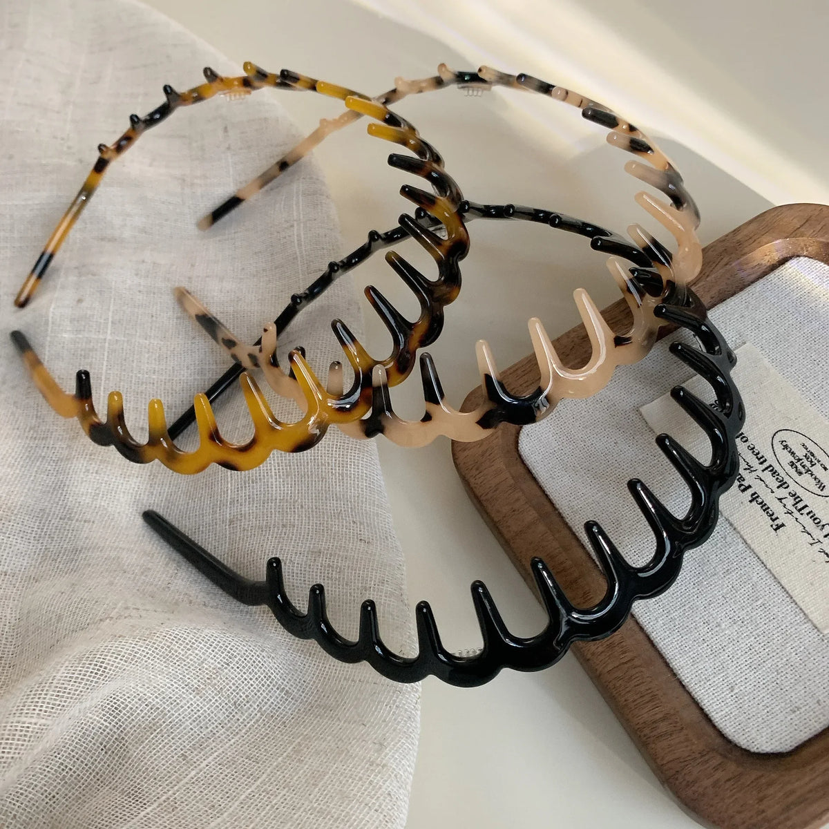 A set of fashion acetate toothed headbands in black and amber are displayed on a wooden board.