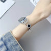 A close-up of a silver watch strap with a diamond four-leaf clover charm on a wrist, next to a denim sleeve.