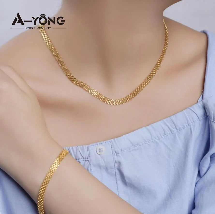 A gold plated chain necklace worn by a woman against a light blue shirt.
