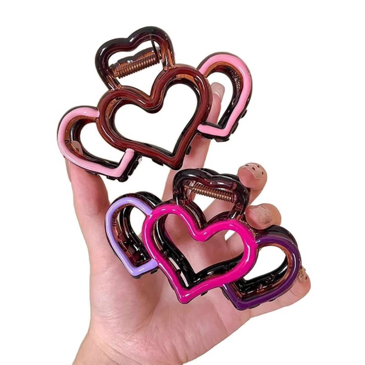 A hand holds several heart-shaped hair claws in shades of brown, pink, and purple.
