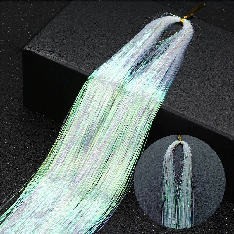 Long, fine, iridescent light green hair extensions with rainbow glitter strands displayed on a black surface.