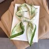 A light green and white floral silk scarf tied in a bow, displayed on a beige blazer.
