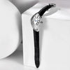 A silver-cased fashion quartz wristwatch with a Roman dial and black leather strap resting on a white surface.