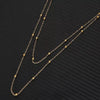 Gold chain body jewelry featuring small gold beads and links displayed against a dark background.