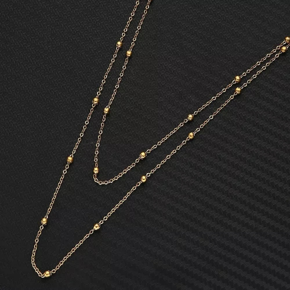 Gold chain body jewelry featuring small gold beads and links displayed against a dark background.