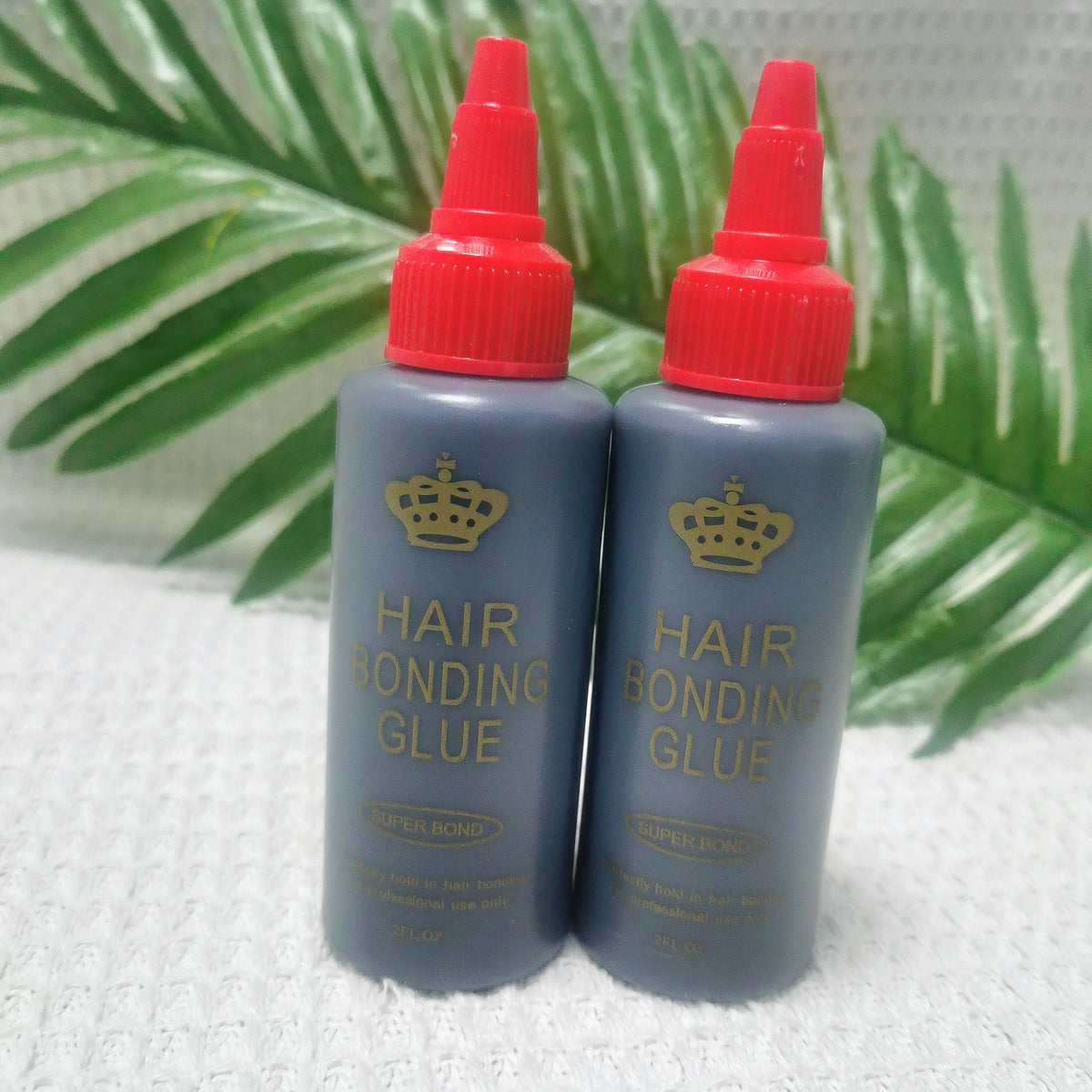 Two bottles of Super Bond Hair Bonding Glue with red caps set against a green leaf background