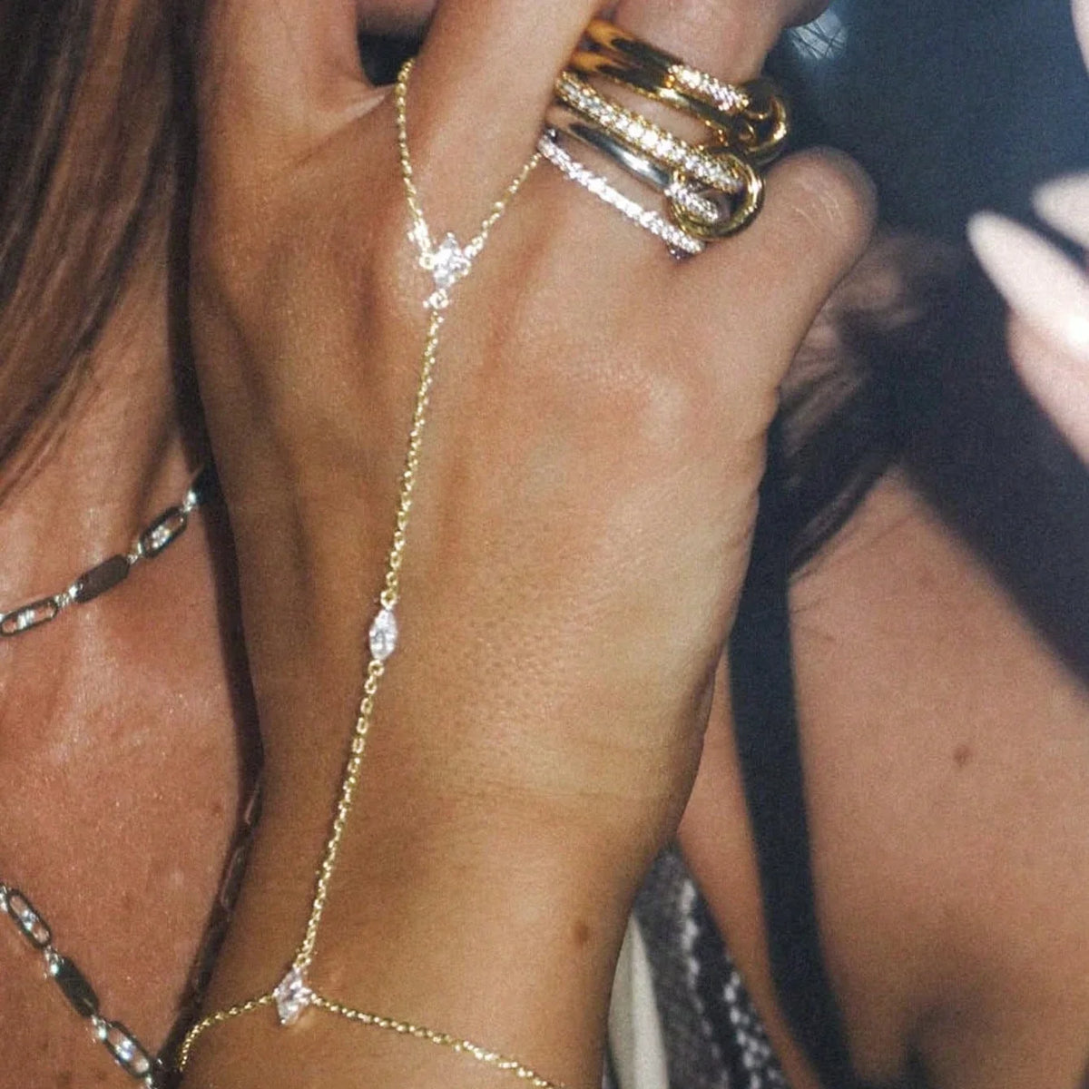 Close-up of a hand wearing multiple gold and diamond ball link finger bracelets