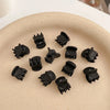A set of black adjustable hair claw clips arranged on a light beige plate.