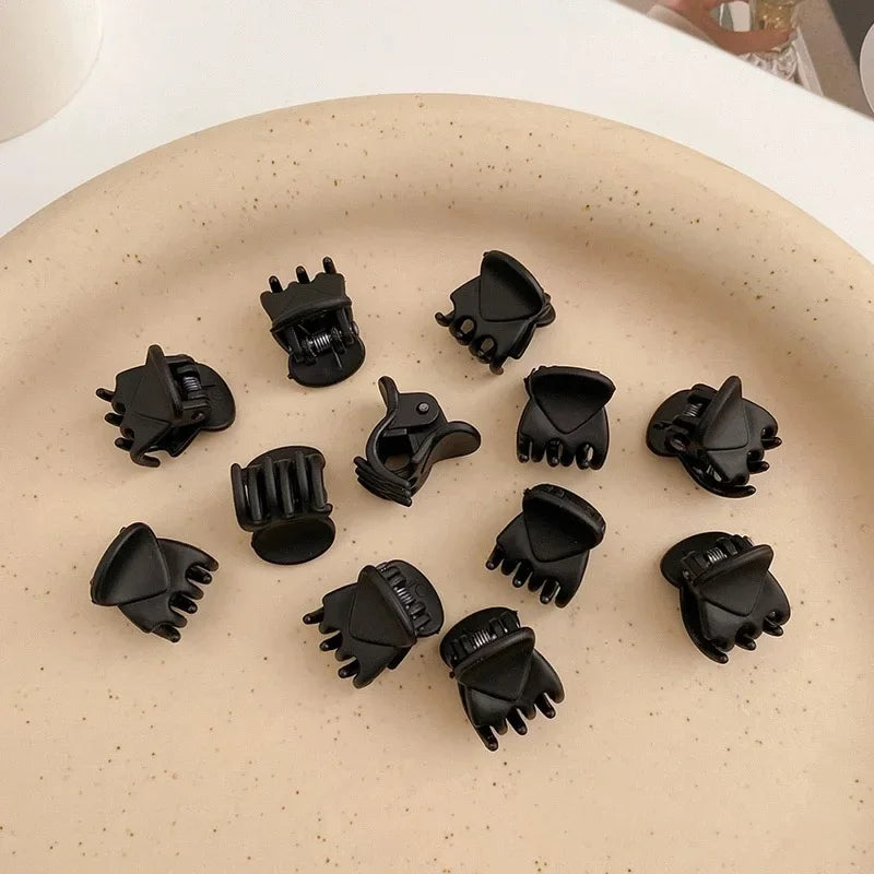 A set of black adjustable hair claw clips arranged on a light beige plate.