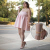A woman models a pink dress and gold snake chain anklets outdoors.