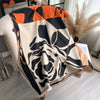 A beige and black floral patterned scarf or shawl draped over a chair.