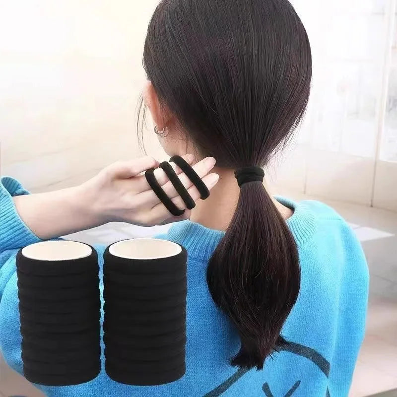 A woman ties a black elastic hair tie into a ponytail on the back of her head.