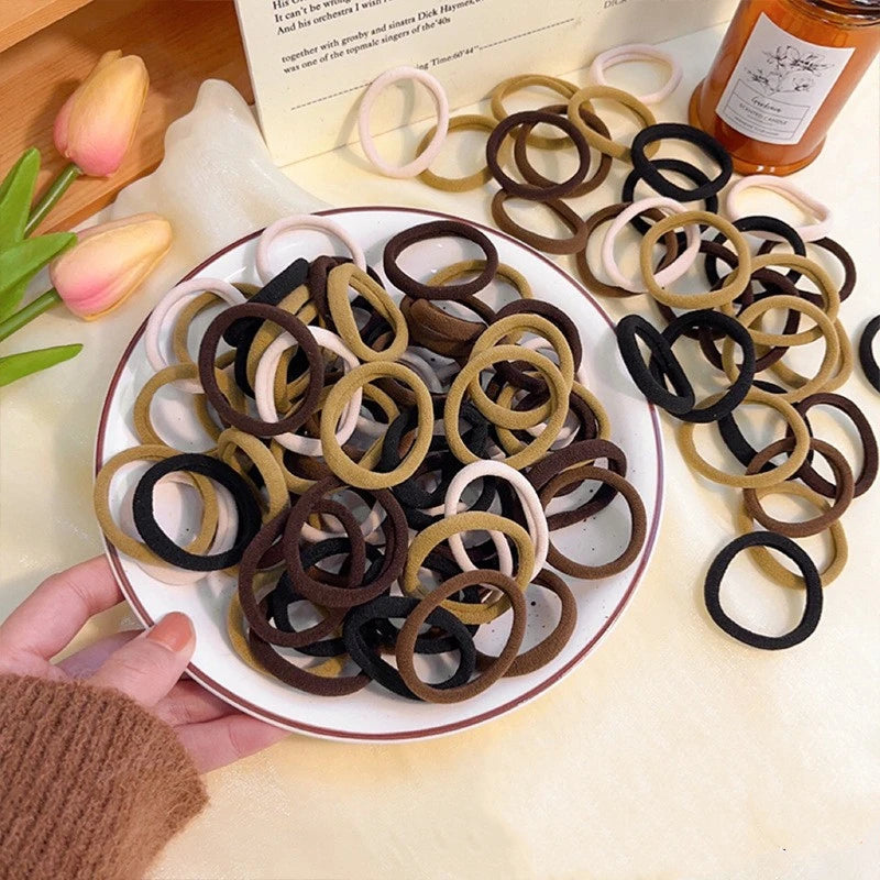 A plate of various colored elastic hair bands, including black, brown, and beige, are displayed on a light surface.