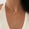 Un collier de perles minimaliste en or porté au cou d'une femme sur un fond neutre.