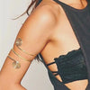 A close-up of a woman's arm showing six gold-plated swirl cuff armbands worn on the wrist and forearm.