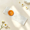 A white lace headband with an orange button and several daisy flowers on a light background.