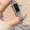 A close-up shot of a vintage gold stainless steel quartz watch with a black face and silver bracelet resting on a beige textu