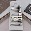 Un set de ocho pinzas para el cabello de metal plateado para flequillo y accesorios, exhibidos en una caja blanca.