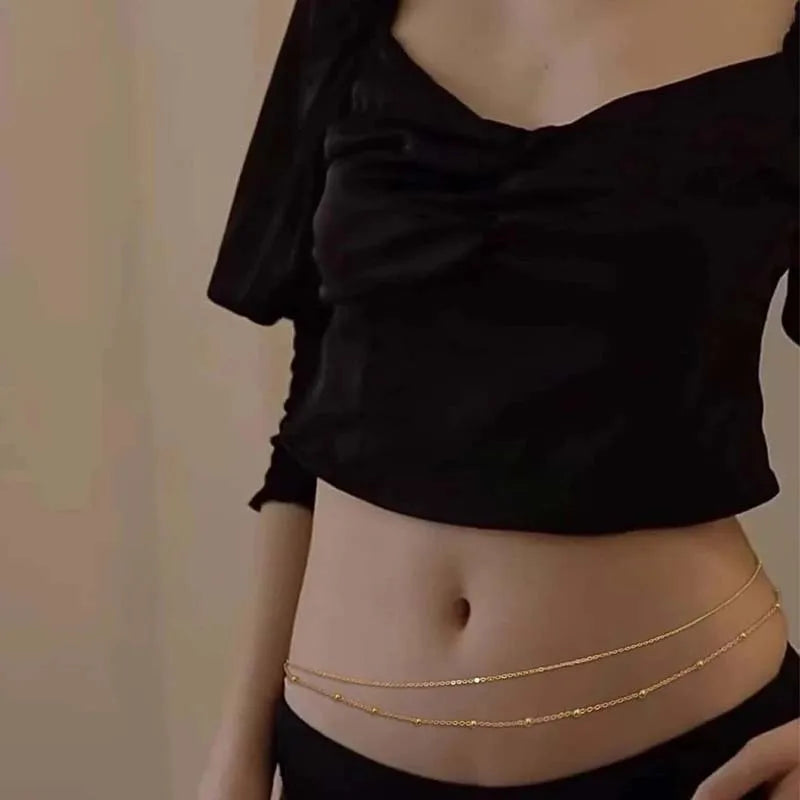 A close-up of a woman wearing gold layered metal belly chains on her abdomen.