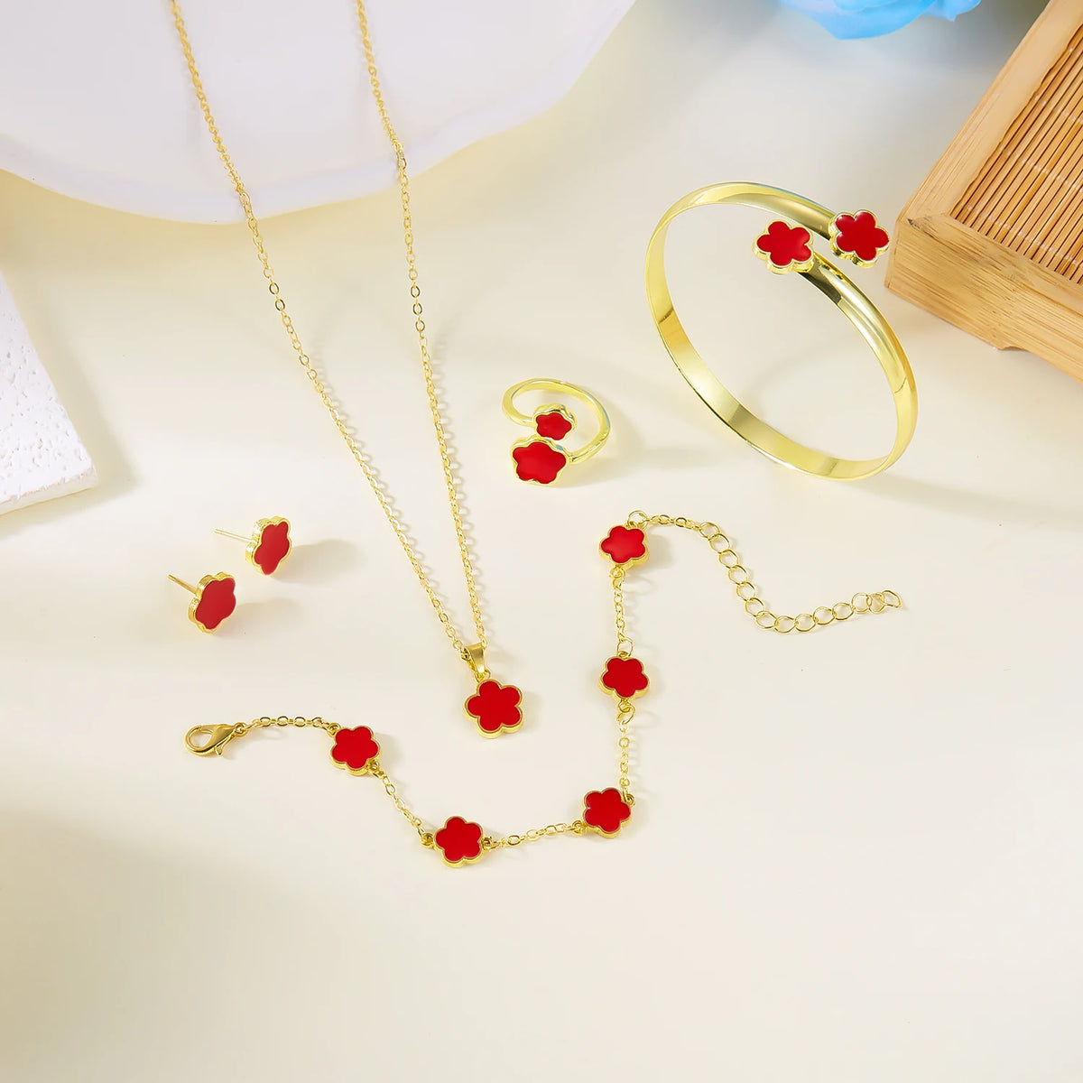 A set of five gold-colored bracelets featuring red enamel plum blossoms displayed on a light background.